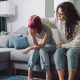 Adult curly haired woman consoling, stroking teen girl, sitting on a sofa. (Getty Images)
